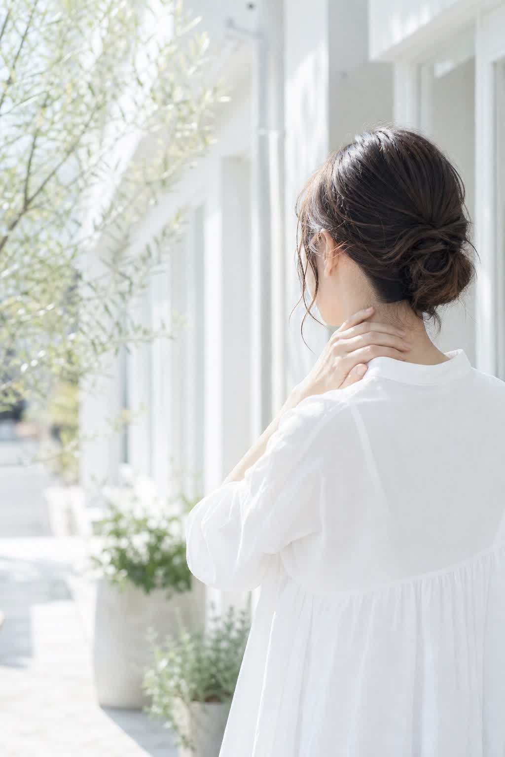 首元に手を添えた白い服の女性と明るいサロン外観の症状案内イメージ